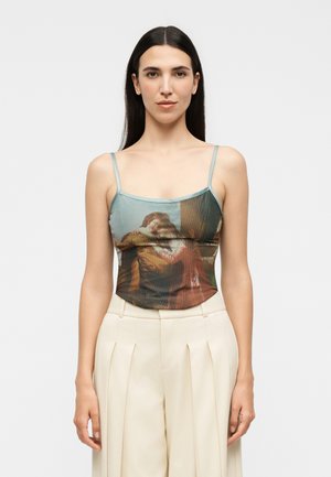 Žena s dlhými tmavými vlasmi nosiaca top na tenkých ramienkach s potlačou klasickej umeleckej scény, v páre s béžovými vysokými plisovanými nohavicami.