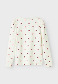 Chemise à manches longues en coton crème avec un col rond, ornée d'un motif répété de petits cœurs rouges et de détails de manches bouffantes.