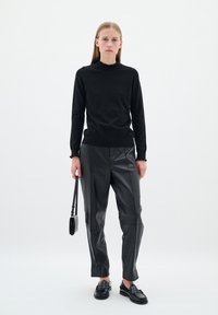 Svart tröja med volangkrage, tillsammans med högmidjade svarta läderbyxor. Modellen håller en liten svart väska och bär loafers.