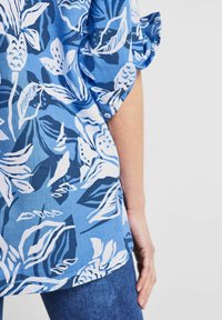 Blue floral blouse featuring a mix of dark and light blue leaves and flowers against a light blue background, short sleeves, and a relaxed fit.