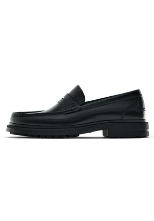 Mocassin en cuir noir avec une épaisse semelle en caoutchouc et un détail de bride penny classique, vu de côté sur fond blanc.