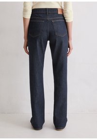 Dunkelblaue Jeans mit geradem Schnitt, mittlerer Bundhöhe, einem beige Lederpatch auf der Rückseite und zwei hinteren Taschen mit sichtbaren Nähten.