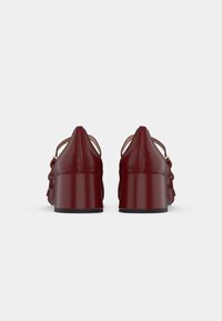 Red patent leather high-heeled shoes with a glossy finish, open sides, and a chunky heel. Features bows on the outer sides.