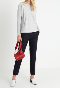 Hellgrau gestrickter Pullover, marineblaue maßgeschneiderte Hose, weiße Blockabsatz-Mules und eine kleine rote Handtasche mit "Calvin Klein"-Logo und verstellbarem Trageriemen.