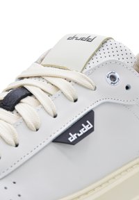 Gray leather sneaker with beige accents, textured surface, rounded toe, visible stitching, and lace-up fastening. Features logo detail.