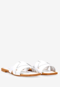 Sandales blanches à lanières croisées en matériau synthétique lisse et semelle plate marron clair, présentant un design minimaliste.