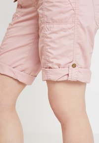 Jasnoróżowe, krótkie spodenki do kolan wykonane z lekkiego materiału, z wywiniętymi mankietami i guzikiem na krawędzi.