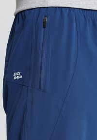 Marineblau Shorts aus leichtem Material, mit einer seitlichen Reißverschlusstasche und dem "BIDI BADU"-Logo in Weiß. Glatte Textur mit lässiger Passform.