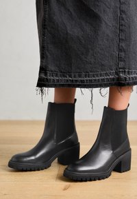 Svarta läderankelboots med elastiska sidopaneler, blockklackar och strukturerade sulor. Bärs med en slitna svart denimkjol.