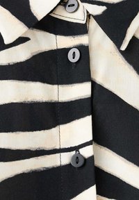 Chemise rayée zèbre noire et blanche avec des boutons noirs et un col pointu, montrant un gros plan de l'avant boutonné.