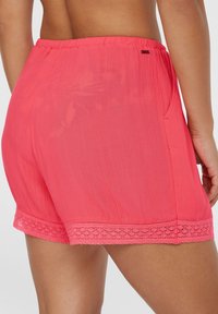 Coral pink shorts with an elastic waistband, lace trim at the hem, and side pockets. Made from a lightweight, textured fabric.