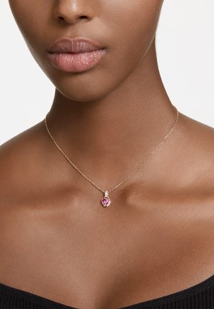 Collier en chaîne dorée avec un pendentif en forme de cœur, doté d'un centre en gemstone rose et de petites accents, reposant sur une peau de teinte lisse.