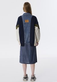 Denim en stoffen jas met een marineblauwe, kaki en crème kleurblokkering, met een bruine leren label en geribde manchetten.