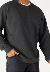 Sudadera de cuello redondo de color gris oscuro, hecha de un tejido suave, con mangas largas y un corte relajado, combinada con jeans oscuros.