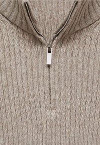 Pull en tricot côtelé beige avec un col haut et une fermeture éclair à mi-hauteur. Présente une texture lisse et un détail de fermeture éclair métallique.