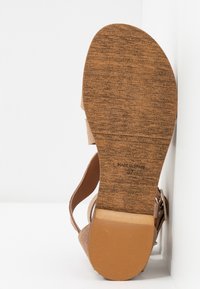 Sandalias marrones claras con suela de corcho texturizada, correa ajustable y parte superior de tela suave. Diseño plano ideal para el uso diario. Fabricadas en España.