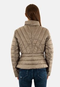 Doudoune taupe, présentant un motif matelassé vertical, un col haut et une taille cintrée, assortie à un jean bleu foncé.