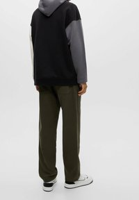 Sudadera con capucha de diseño a bloques de color en negro, gris y beige. Combinada con pantalones verde oliva y zapatillas blancas.