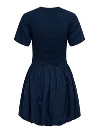 Tumesinise lühikeste varrukatega kleit, millel on fitted smockitud korsett ja kogutud õhupalli stiilis seelik, nähtav tagantpoolt.