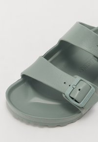 Sandale Birkenstock en vert clair, fabriquée en matériau synthétique texturé. Deux larges brides avec boucle réglable et semelle intérieure profilée.