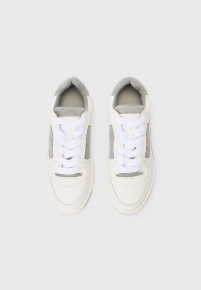 Ein Paar weiße und graue Sneakers mit weißen Schnürsenkeln, von oben auf einem einfarbigen hellgrauen Hintergrund betrachtet.