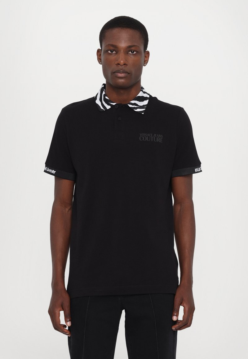Black polo shirt with zebra-striped collar and embroidered logo on chest. Short sleeves with accents at cuff. Smooth cotton material.