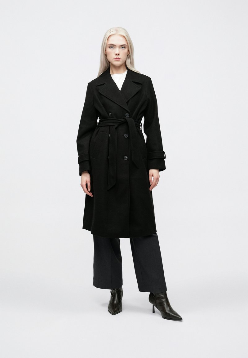 Cappotto nero con un design doppiopetto, vita cinturata e ampi rever. Presenta tasche a pattina e una linea dritta, lunga fino al ginocchio.