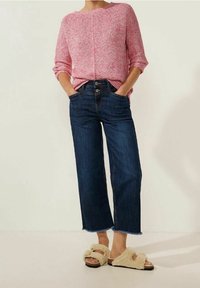 Rosa texturerad stickad tröja, högmidjade mörkblå korta jeans och beige fluffiga sandaler med banddesign. Avslappnad outfit med ledig passform.