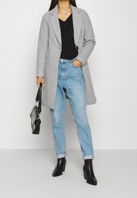 Grijze jas van een wolblend met een enkele knoopsluiting en reverskraag, gecombineerd met een zwarte trui en lichtblauwe jeans met hoge taille. Zwarte enkellaarzen.