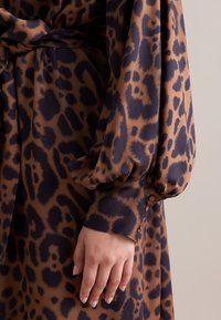 Abito con stampa leopardata in marrone e blu navy, caratterizzato da maniche voluminose e dettagli con bottoni ai polsini, realizzato in un tessuto morbido.