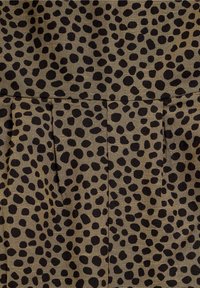 Tissu marron avec un motif de taches noires, présentant des plis près du bas pour une texture et un détail de conception ajoutés.