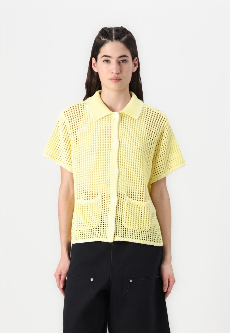 Camicia gialla a maniche corte con un design a rete testurizzata, dotata di colletto, chiusura frontale a bottoni e due tasche frontali.
