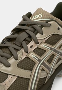 Asics løpesko med mesh-overdel i mørkebrunt og beige, med tonede overlags, flate lisser og polstret krage for komfort.