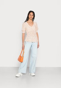 Blusa de manga curta com padrão floral em branco e laranja, combinada com calças de cintura alta em azul claro e uma pequena bolsa laranja.