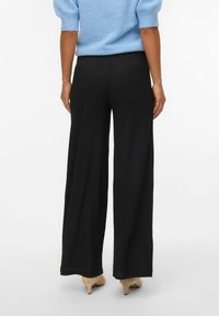 Črne široke hlače z teksturirano površino, ki imajo udoben pas in so kombinirane s svetlimi petami.