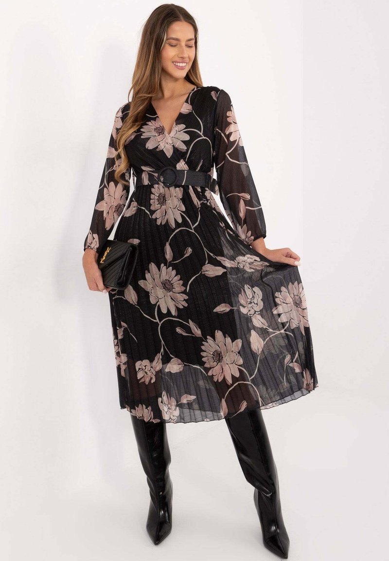 Schwarzes Midikleid mit floralem Muster, langen Ärmeln, plissierter Textur und tailliertem Schnitt. Kombiniert mit kniehohen schwarzen spitzen Stiefeln und einer kleinen Tasche.