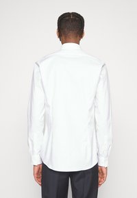 Chemise blanche à manches longues avec coupe droite et poignets boutonnés, fabriquée en tissu lisse. Aucune motif visible, conçue pour un look formel.