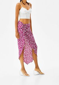 Lila blommig omslagskjol med höga sidoklyftor, strukturerad tyg, knuten front, matchad med klara kilklackar och en vit kort topp.