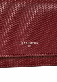 Portefeuille en cuir bordeaux texturé avec un motif tissé subtil, arborant un logo de marque embossé en argent. Forme compacte avec des détails de couture soignés.