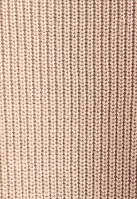 Strickstoff in sanftem Beige mit vertikaler Rippstruktur. Das Garn weist subtile Variationen auf, die ein glattes und einheitliches Erscheinungsbild erzeugen.