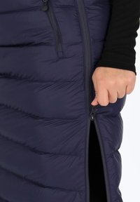 Tummansininen alushame, jossa on vaakasuora tikkauskuvio, sivuilla vetoketju ja tiukka leikkaus. Materiaali vaikuttaa pehmeältä ja sileältä.