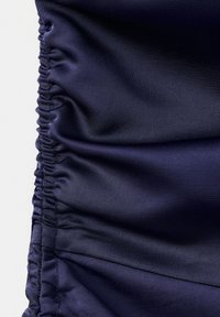 Tissu satin bleu foncé avec couture élastique froncée le long du bord gauche créant des plis lisses et brillants.