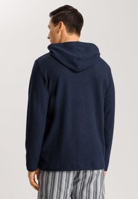 Sudadera con capucha en color navy, de mangas largas, textura suave, diseño liso, con una costura trasera y un ajuste relajado, combinada con pantalones a rayas.