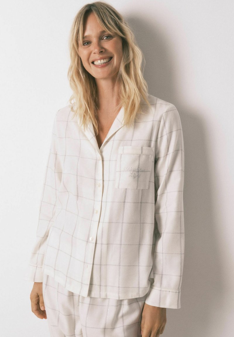 Hvid pyjamas sæt med grå rutemønster, lange ærmer, knaplukning, brystlomme, lavet af blødt stof. Matching bukser ses nedenfor.