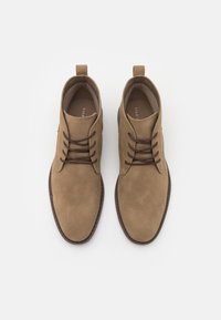 Brune suede ankelstøvler med mørkebrune snørebånd, rund form og trækstrop. Glat tekstur og kontrasterende syning.