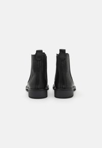 Botas de tobillo de cuero negro con paneles laterales elásticos, suela plana y tacón resistente. Costuras visibles que acentúan los lados.