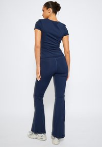 Marinblå atletisk topp med korta ärmar och matchande utsvängda byxor, tillverkad av stretchmaterial; har logotyp på baksidan. Silverfärgade sneakers.