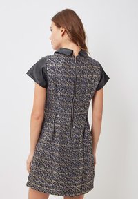 Vestido corto con tela estampada en azul y dorado, mangas cortas de cuero y cierre con cremallera en la parte posterior. Textura suave con silueta ajustada.