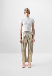 Biely, krátky zip-up top, metalicky zlaté široké nohavice a svetloružové tenisky. Hladká textúra, minimalistický dizajn.