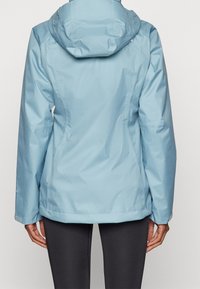 Vaaleansininen vedenpitävä takki hupulla, jossa on sileä pinta, säädettävät hihansuut ja saumadetaileja selässä ja harteilla.